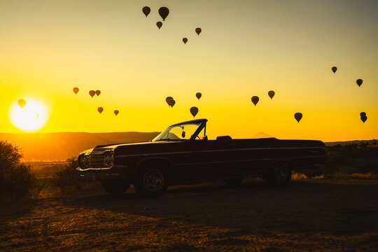 Classic Vintage Convertible Car at Sunrise with Hot Air Balloons in Cappadocia Landscape