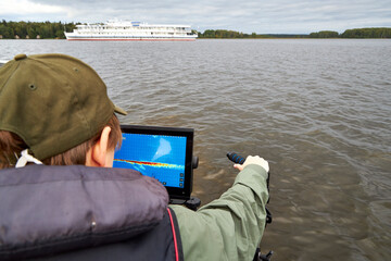 Fisherman steering boat while looking at fishfinder screen on a lake. Modern angling technology...