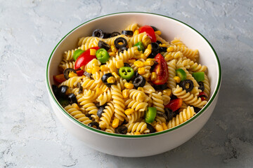 Fresh homemade colorful vegan fusilli pasta salad with olive, corn, tomato and jalapeno close-up in...