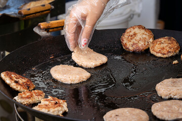 Fresh fish cutlet in a frying pan grill. Barbecue festival in the city park. Street fast food. A large round  grill is roasting fish patties. 