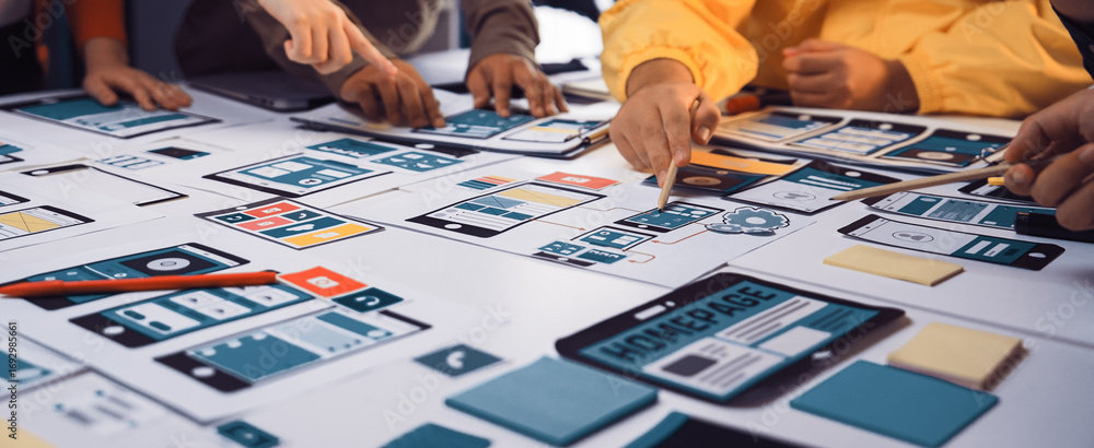 Poster a diverse team collaborates during a design session, pointing at mobile app wireframes and sketches 