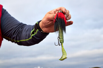 Close-up of fisherman hand holding colorful fishing lure with treble hook. Angling equipment detail...