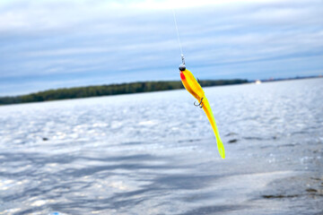 Colorful fishing lure with treble hook hanging on line above water surface. Outdoor angling...