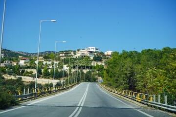 A view from the New National Road of Crete, showing the Pantanassa bridge. The road curves slightly, leading toward a collection of dwellings dot on a hillside with a white building on top. 