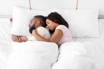 Calm cute peaceful young african american woman hugs man and sleeps on comfort bed together in...