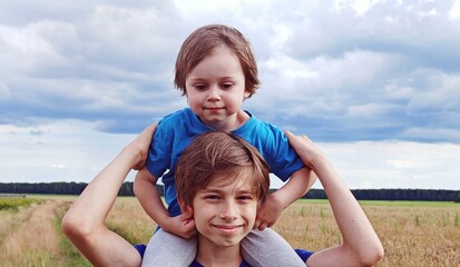 teenage brother plays with his younger brother in nature in summer day. Brother love. Concept...