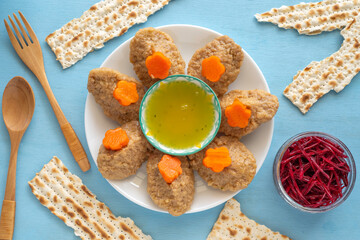 Traditional food for Jewish holiday Pesach or Passover on blue wooden background. Matzah pieces, gefilte fish, fish broth, grated beetroot on wooden table. Top view.
