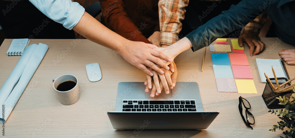 Poster a group of professionals joins hands over a laptop in an office workspace, symbolizing teamwork and 