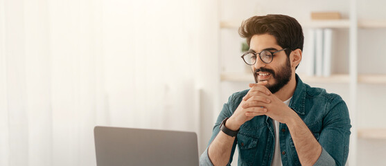 Handsome arab entrepreneur working on laptop computer at home office, sitting at workplace, empty...