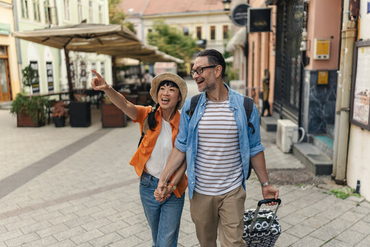 Smiling tourists in their forties holding hands and walking through a charming city street, enjoying sightseeing, love, and travel together