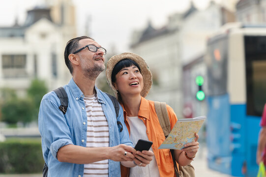 Smiling tourists in their forties holding a map and smartphone while sightseeing in the city, enjoying travel and exploring new destinations