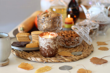 Lit candles, cookies, chocolate, nuts, tea, wine, pumpkins, books, reading glasses and autumn leaves on the table. Autumnal hygge at home. Selective focus. 