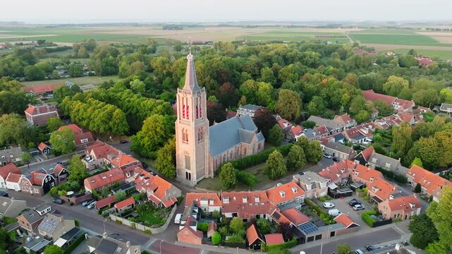 Iconic Dutch protestant church in a small city surrounded by residential houses with orange tile rooftops, aerial orbit