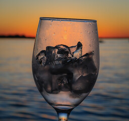 View of the sun setting over the Chobe river through a wine glass filled with ice