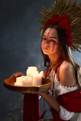 Mysterious woman with tribal face paint and decorative headdress holds a tray of candles in a...