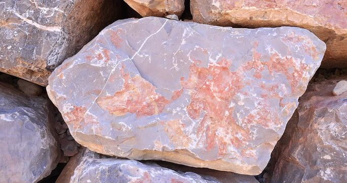 Closeup gray and rust color small rock with patches and streaks of white mineral in dry stack wall with larger colorful stones 4k