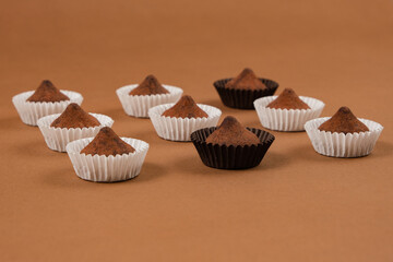 Top view of chocolate truffles in contrasting white and dark paper cups on warm brown paper. Great for use in dessert packaging, food branding visuals, or chocolate-themed advertising.