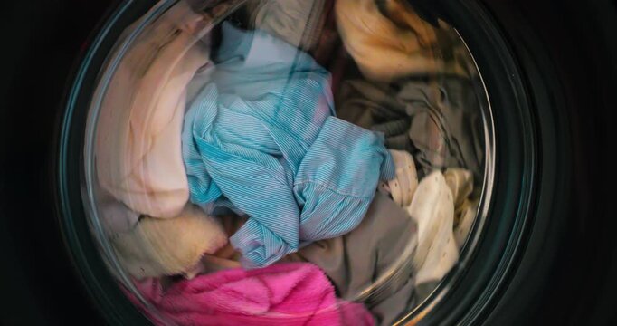 Vibrant wet clothes swirling inside washing machine drum, creating mesmerizing colorful patterns during dynamic spinning cycle with rhythmic fabric movement and rotating textures