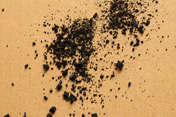 Scattered coal chips and dust on brown cardboard as texture