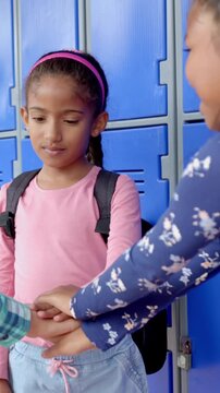 Vertical video: Meeting at blue lockers three elementary schoolgirls stacking hands sharing moment