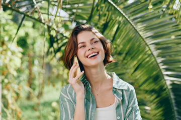 Woman on a phone outdoors in a sunny garden, smiling with confidence, natural light, casual style, fresh air, nature backdrop, calm mood, everyday moment, upbeat vibe