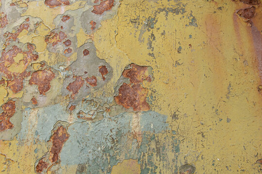 Old metal surface with peeling yellow and green paint and rust areas and rough and aged texture