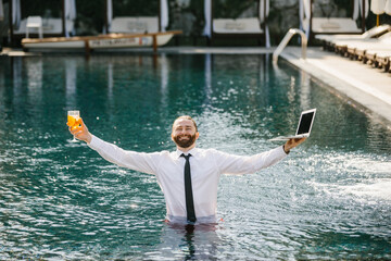 Businessman working remotely from swimming pool with laptop and cocktail