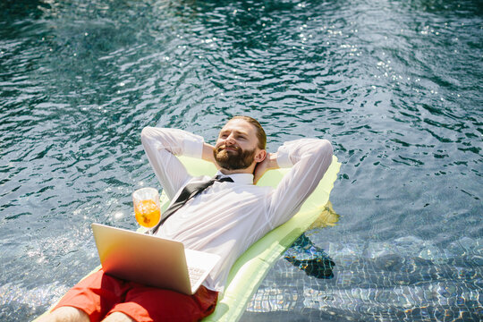 Businessman relaxing in swimming pool with laptop and cocktail
