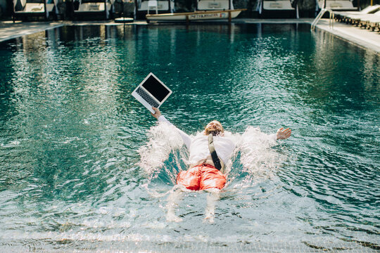 Businessman falling into swimming pool with laptop in hand