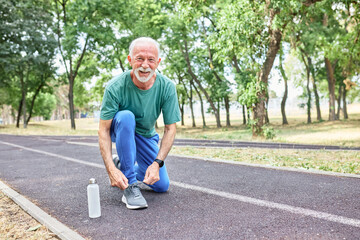 Portrait of a happy active elderly senior man posing fixing shoelace lace on his running shoe after...