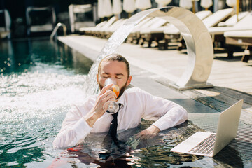 Businessman drinking cocktail in swimming pool with laptop
