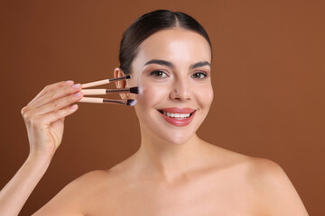 Beautiful woman with makeup brushes on brown background