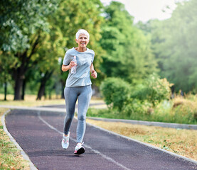 Smiling active mature elderly woman jogging running and holding a water bottle  in the park