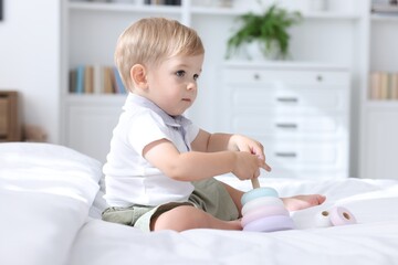 Fototapeta premium Cute little baby playing with toy pyramid on bed at home
