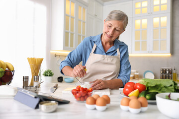 Senior woman cooking at white marble table in kitchen
