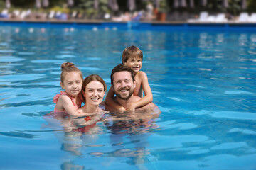 Happy family resting in swimming pool outdoors, space for text