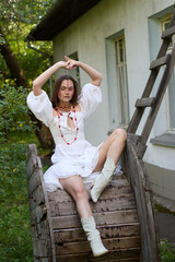 Young woman with decorative face paint in a white dress and boots sitting on a wooden reel against...