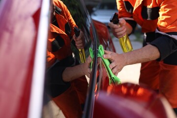 Man wiping car with green microfiber rag outdoors, closeup