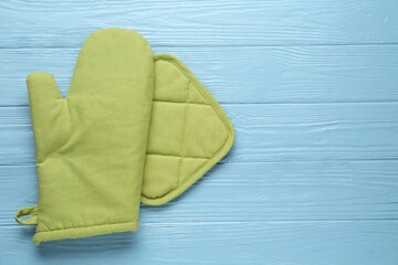 Green oven glove and potholder on light blue wooden table, flat lay. Space for text