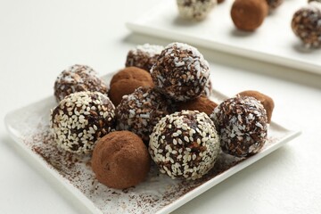 Tasty chocolate candies with cocoa powder, nuts and sesame seeds on white table, closeup