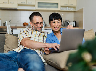 Portrait of a lovely young couple using a laptop together and having fun sitting on sofa at home