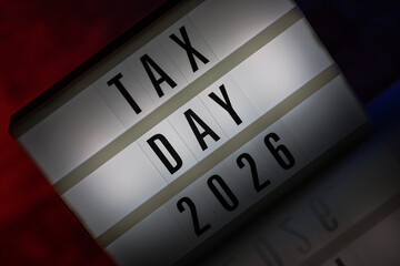 A cinematic lightbox with the words Tax Day 2026 illuminated, placed against a rustic brick...