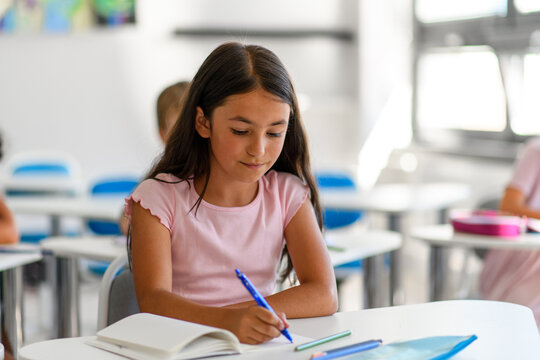 Focused schoolgirl writing notes in classroom. - Powered by Adobe