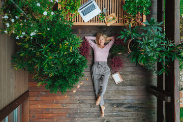 Tpp view of older woman working from homeoffice, lying on wooden patio.