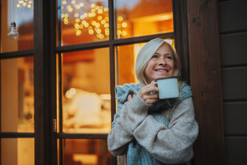 Senior woman enjoying warm tea on terrace during cold autumn evening.