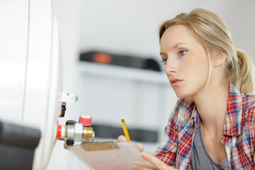 female plumber with clipboard looking at boiler