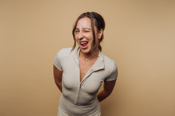 Obraz premium Cheerful woman winks playfully while posing for a casual photo indoors against a neutral backdrop