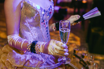 Glamorous performer in sparkling attire serving champagne at a formal event in a lavish setting during the evening