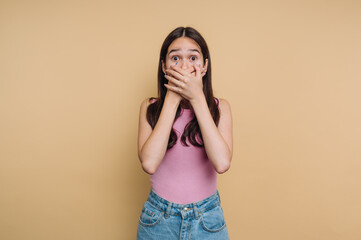 Young girl shows surprise or shock with hands over mouth against a soft yellow background