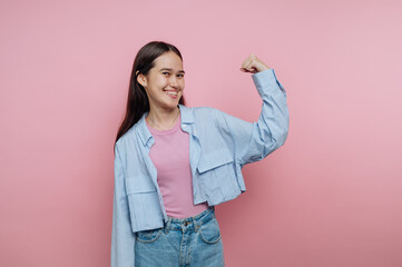 Confident young woman poses with raised arm against a pink backdrop showcasing strength and...